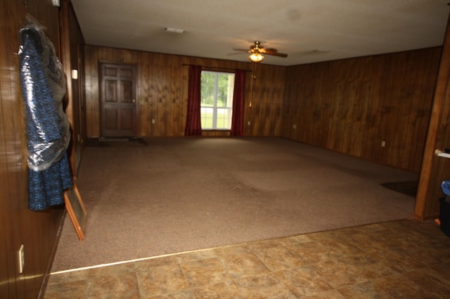 unfurnished room with ceiling fan, wood walls, and carpet floors