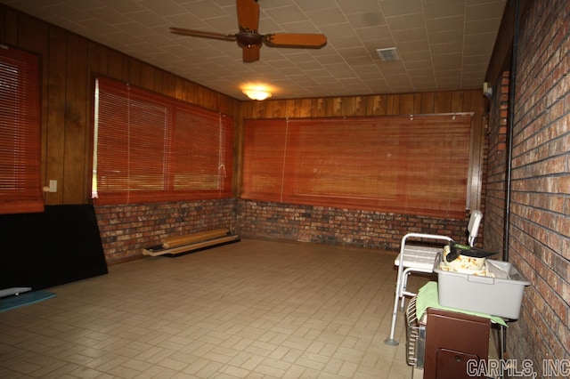 interior space with brick wall, wooden walls, and ceiling fan