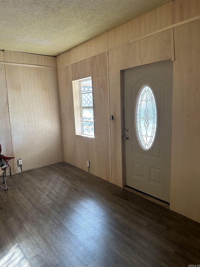 foyer entrance with dark wood-style floors, a textured ceiling, and wooden walls