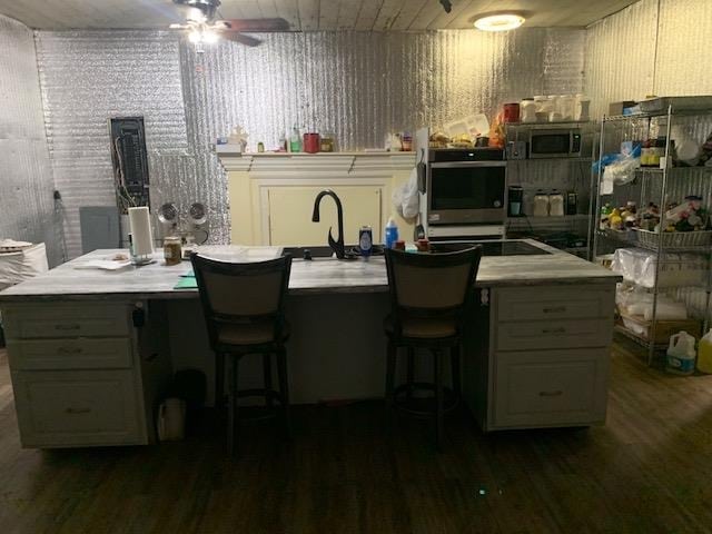 kitchen featuring dark hardwood / wood-style flooring, ceiling fan, an island with sink, and stainless steel appliances