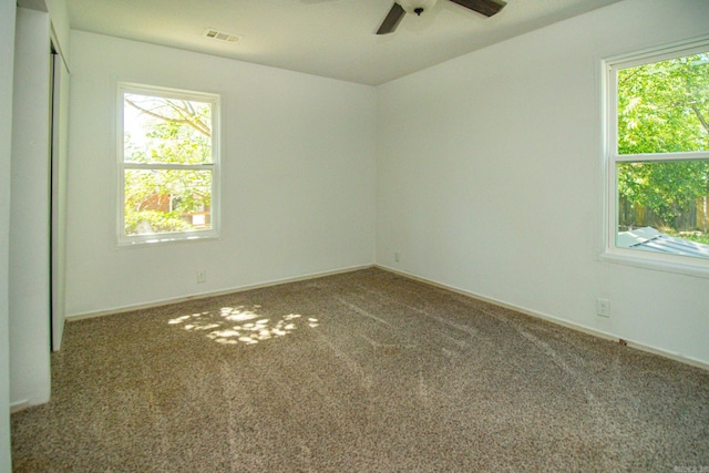 unfurnished room featuring dark carpet, ceiling fan, and a wealth of natural light