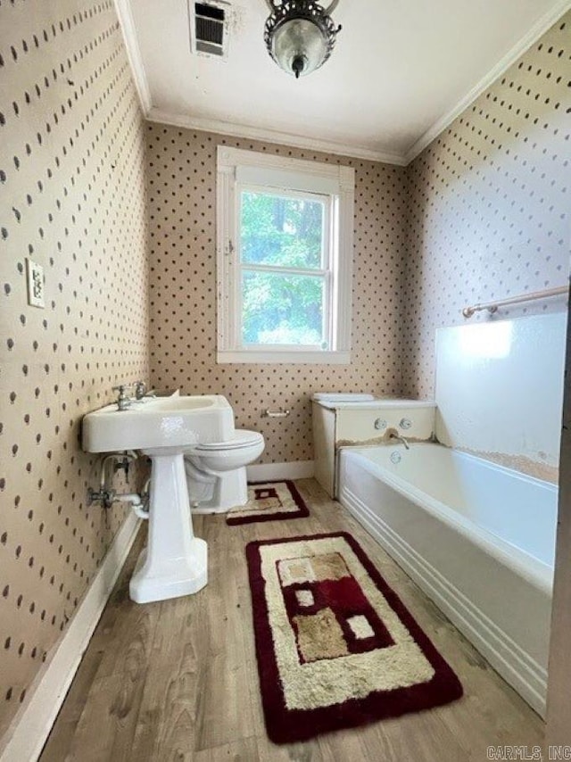 bathroom with hardwood / wood-style floors, crown molding, a bath to relax in, and toilet