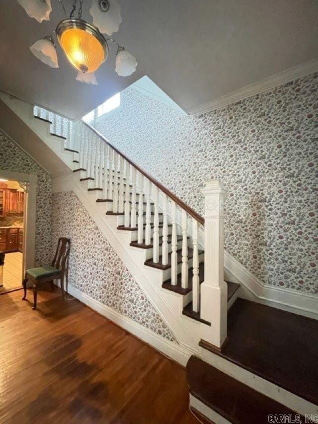 staircase with ornamental molding, a notable chandelier, and hardwood / wood-style flooring