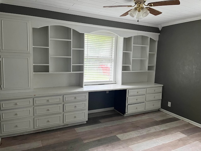 unfurnished office with dark wood-type flooring, ceiling fan, built in desk, and ornamental molding