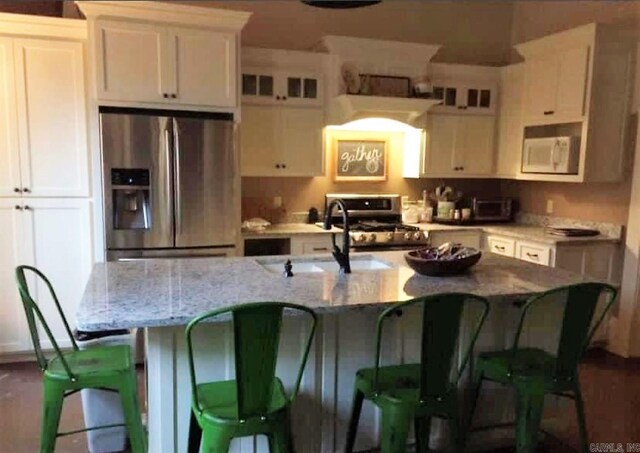 kitchen featuring light stone countertops, white cabinetry, a kitchen island with sink, stainless steel appliances, and a breakfast bar area