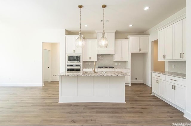 kitchen featuring pendant lighting, appliances with stainless steel finishes, light hardwood / wood-style floors, a center island with sink, and white cabinetry