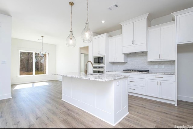 kitchen featuring hanging light fixtures, white cabinets, appliances with stainless steel finishes, light hardwood / wood-style flooring, and backsplash