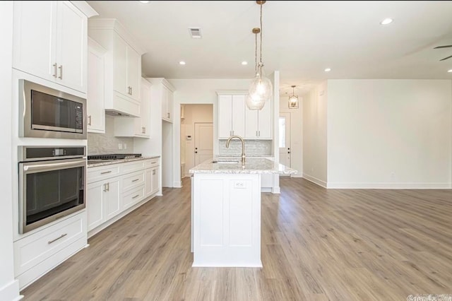 kitchen featuring an island with sink, tasteful backsplash, appliances with stainless steel finishes, and light hardwood / wood-style flooring