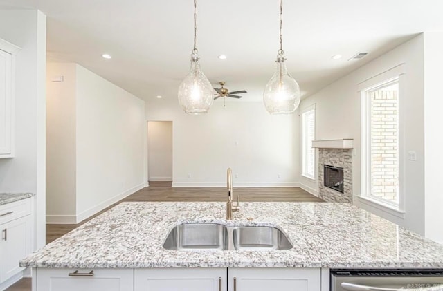 kitchen featuring light stone counters, a stone fireplace, sink, ceiling fan, and hanging light fixtures