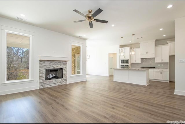 unfurnished living room with ceiling fan, a stone fireplace, and wood-type flooring