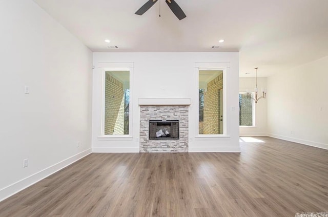 unfurnished living room featuring dark wood-type flooring, ceiling fan with notable chandelier, and a stone fireplace