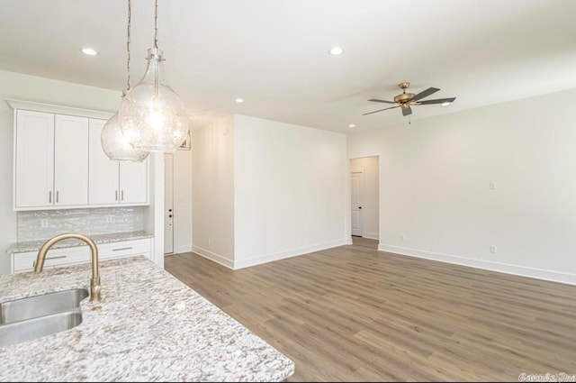 kitchen featuring sink, light stone counters, hanging light fixtures, wood-type flooring, and tasteful backsplash