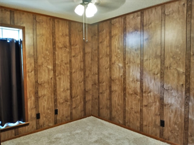 carpeted spare room with ceiling fan and wood walls