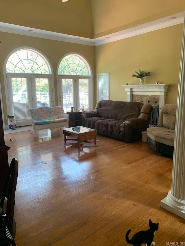 living room with a high ceiling, crown molding, ornate columns, and light hardwood / wood-style flooring