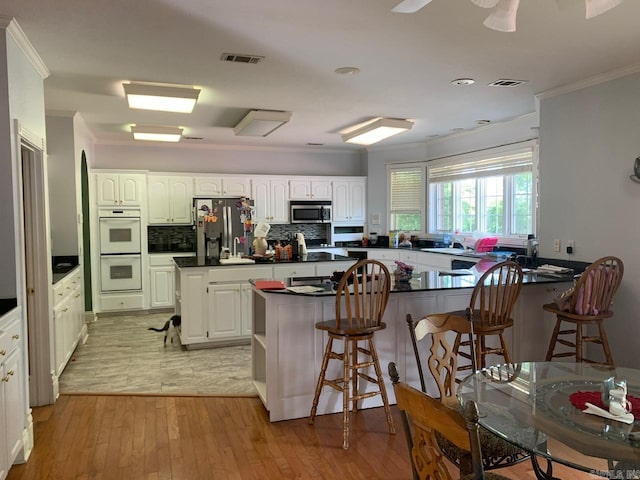 kitchen featuring a breakfast bar, white cabinets, stainless steel appliances, light hardwood / wood-style flooring, and ceiling fan