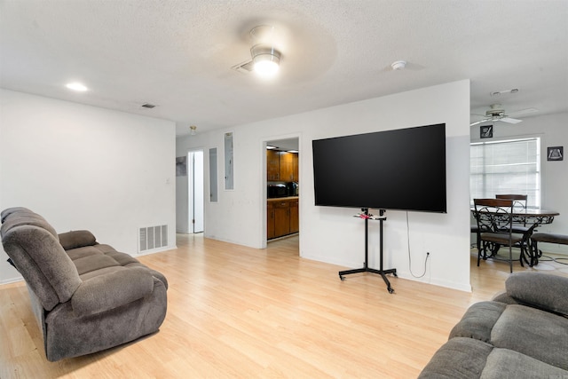 living room with light hardwood / wood-style floors, a textured ceiling, and ceiling fan