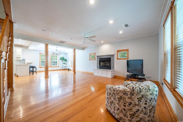 living room with a tile fireplace, ceiling fan with notable chandelier, light hardwood / wood-style floors, and crown molding