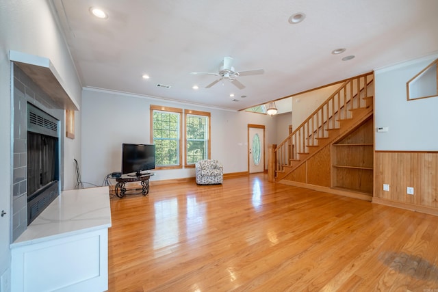 living room featuring crown molding, a fireplace, ceiling fan, and light wood-type flooring