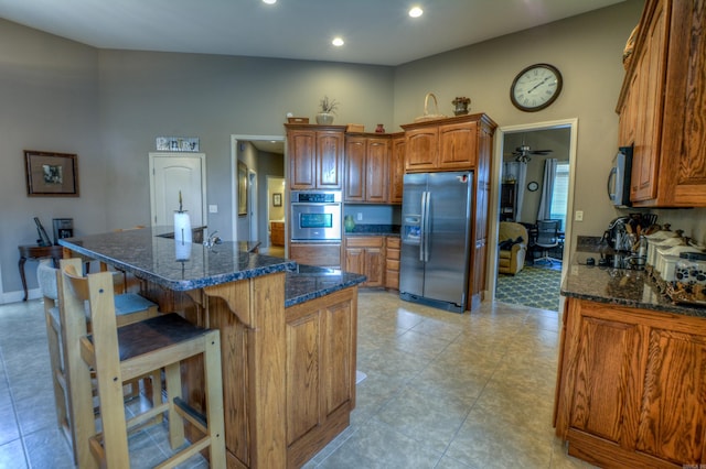 kitchen with ceiling fan, appliances with stainless steel finishes, an island with sink, and light tile floors