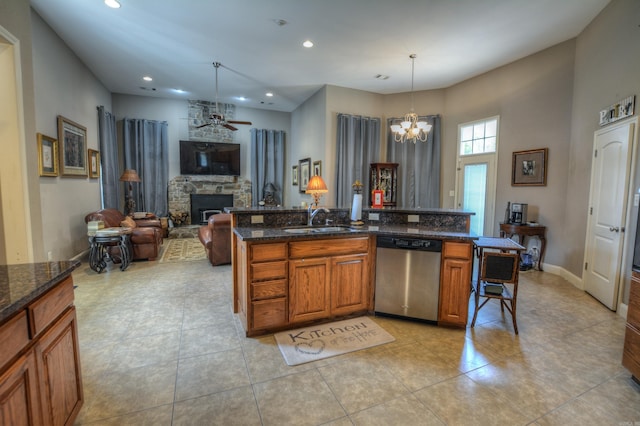 kitchen with decorative light fixtures, light tile flooring, dark stone counters, stainless steel dishwasher, and a stone fireplace