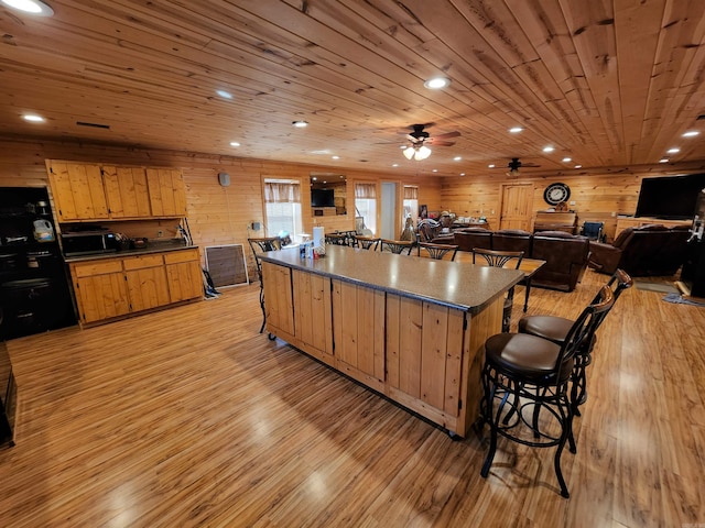 kitchen with a kitchen bar, wooden walls, ceiling fan, and light hardwood / wood-style flooring