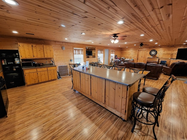 kitchen featuring ceiling fan, light hardwood / wood-style flooring, wooden ceiling, wood walls, and a kitchen bar