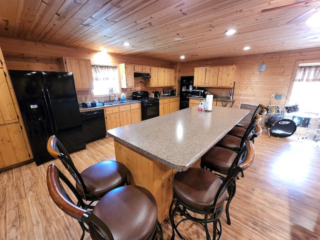 kitchen with light hardwood / wood-style flooring, wood walls, and black appliances