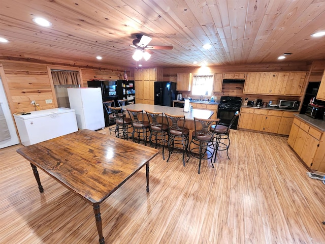 dining area featuring ceiling fan, light hardwood / wood-style floors, sink, wood walls, and wooden ceiling