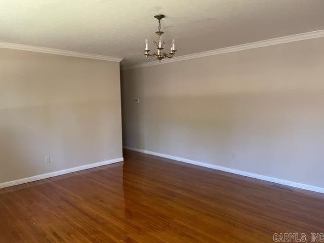 spare room featuring crown molding, dark wood-type flooring, and an inviting chandelier