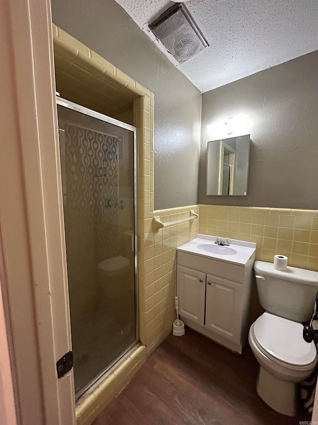 bathroom featuring toilet, large vanity, hardwood / wood-style flooring, a shower with door, and tile walls