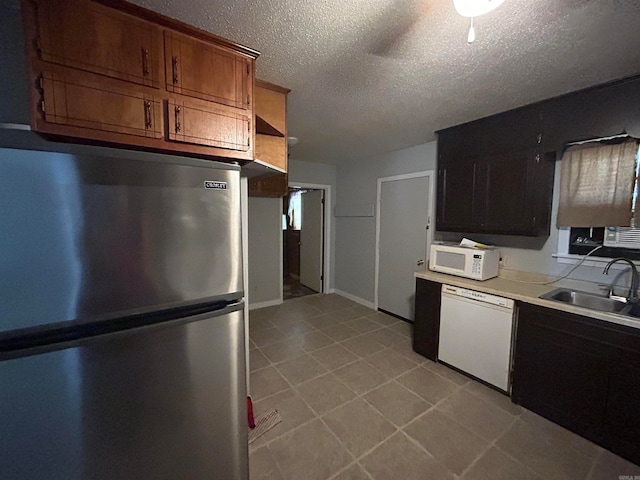kitchen with sink, white appliances, light tile floors, and a textured ceiling