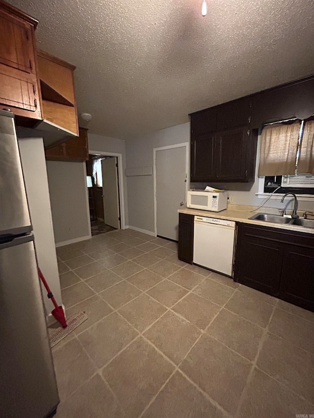 kitchen featuring light tile flooring, a textured ceiling, dark brown cabinets, white appliances, and sink