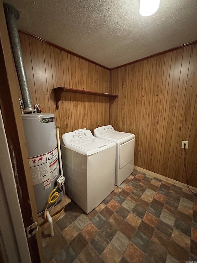 clothes washing area with wood walls, a textured ceiling, washer and clothes dryer, dark tile floors, and water heater