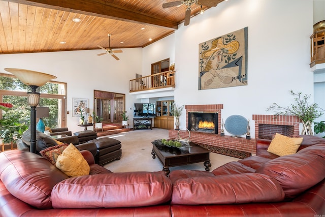 carpeted living room with ceiling fan, beamed ceiling, a fireplace, high vaulted ceiling, and wood ceiling