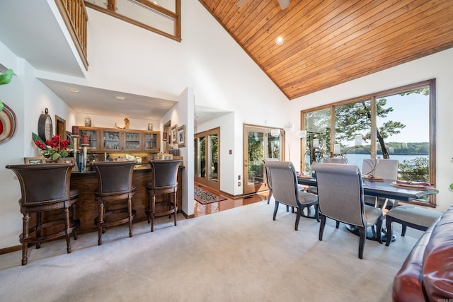 carpeted dining space with high vaulted ceiling, a water view, wood ceiling, and french doors