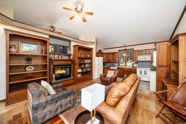 living room with lofted ceiling, ornamental molding, ceiling fan, and light wood-type flooring