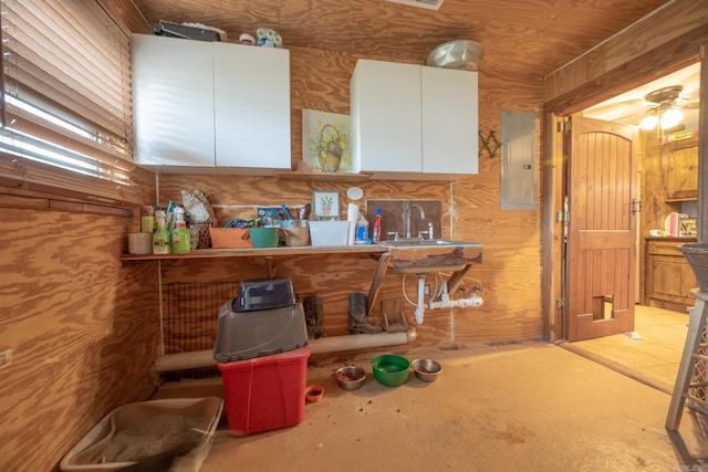 interior space with white cabinets, ceiling fan, sink, and wooden walls