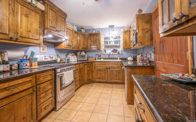 kitchen with hanging light fixtures, stainless steel range with gas cooktop, sink, dark stone countertops, and light tile floors