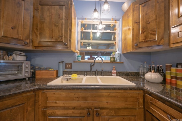 kitchen with hanging light fixtures, sink, and dark stone counters