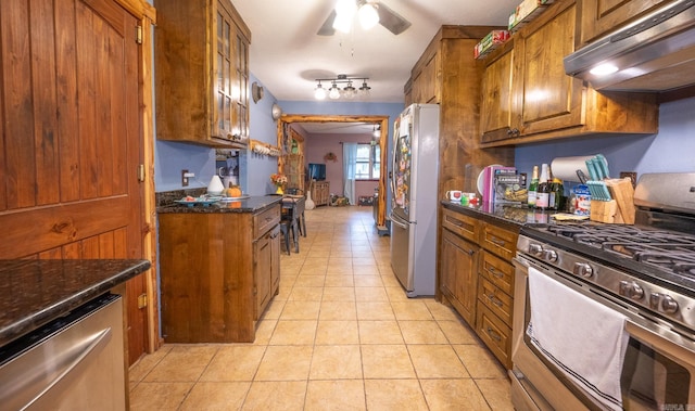 kitchen with ceiling fan, dark stone counters, rail lighting, stainless steel appliances, and light tile flooring