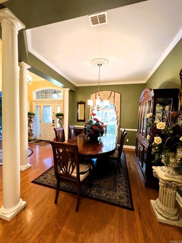 dining area with an inviting chandelier, crown molding, ornate columns, and dark hardwood / wood-style flooring