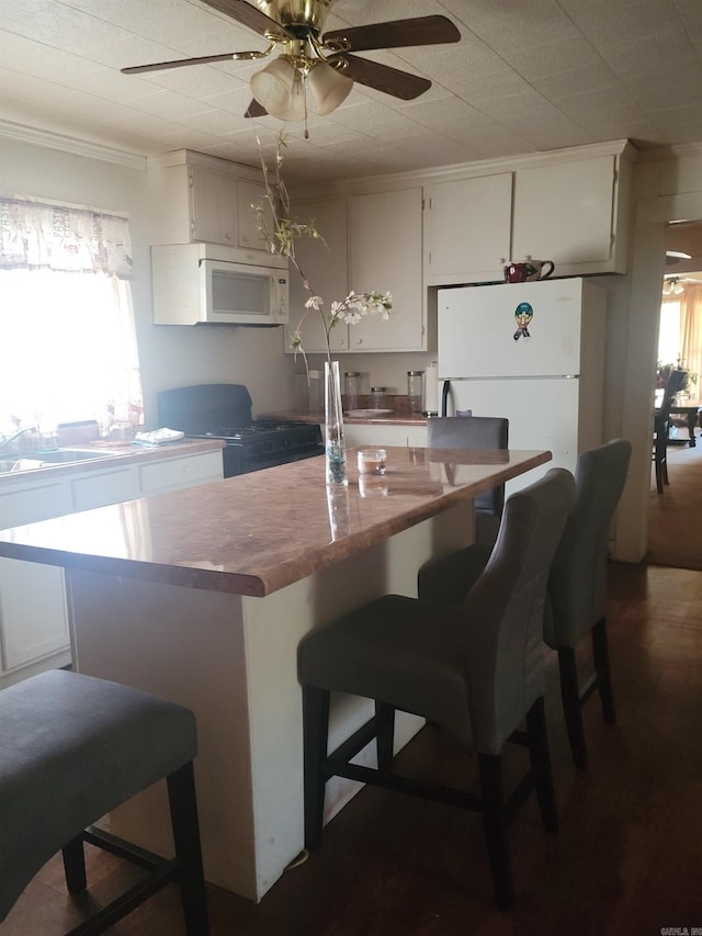 kitchen featuring white appliances, ceiling fan, white cabinets, a breakfast bar, and a center island