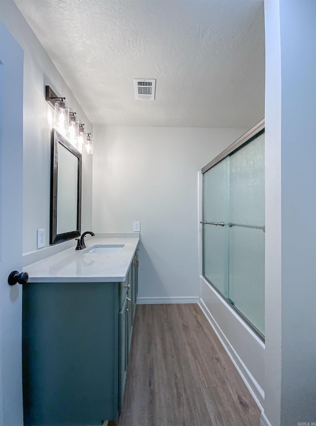 bathroom featuring vanity, a textured ceiling, hardwood / wood-style flooring, and combined bath / shower with glass door