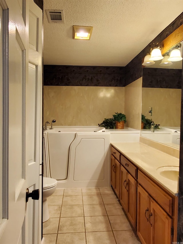 bathroom with tile patterned floors, a tub to relax in, a textured ceiling, toilet, and vanity