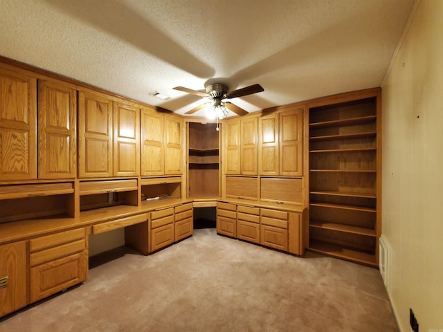 unfurnished office with a textured ceiling, ceiling fan, built in desk, and light carpet