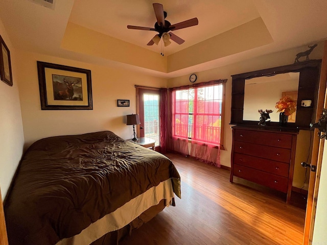 bedroom with ceiling fan, light hardwood / wood-style floors, and a tray ceiling