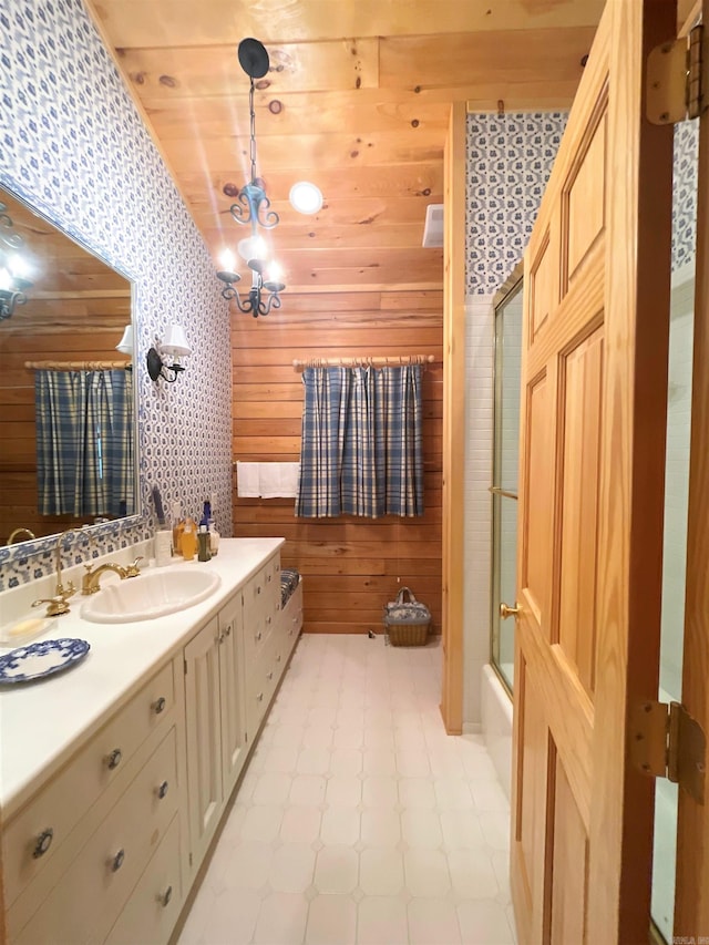 bathroom with shower / bath combination with glass door, wooden walls, vanity, and an inviting chandelier