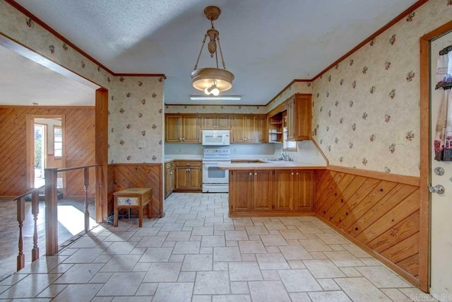 kitchen featuring wood walls, white appliances, hanging light fixtures, and sink