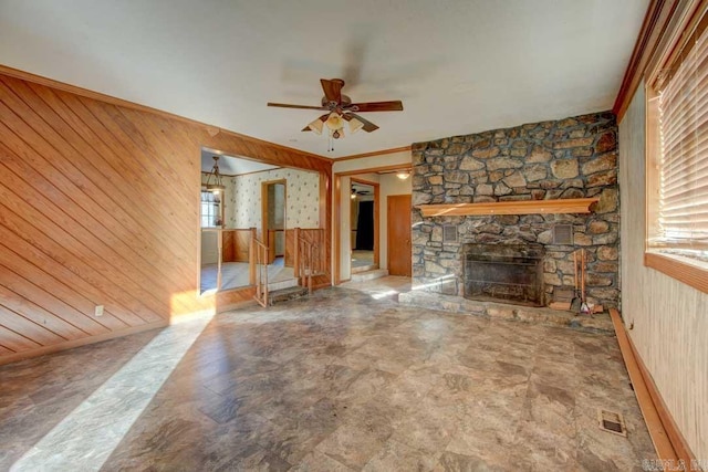 unfurnished living room featuring a healthy amount of sunlight, ceiling fan, a stone fireplace, and wooden walls