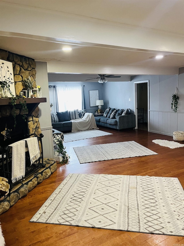 living room featuring a stone fireplace, wood finished floors, and beam ceiling